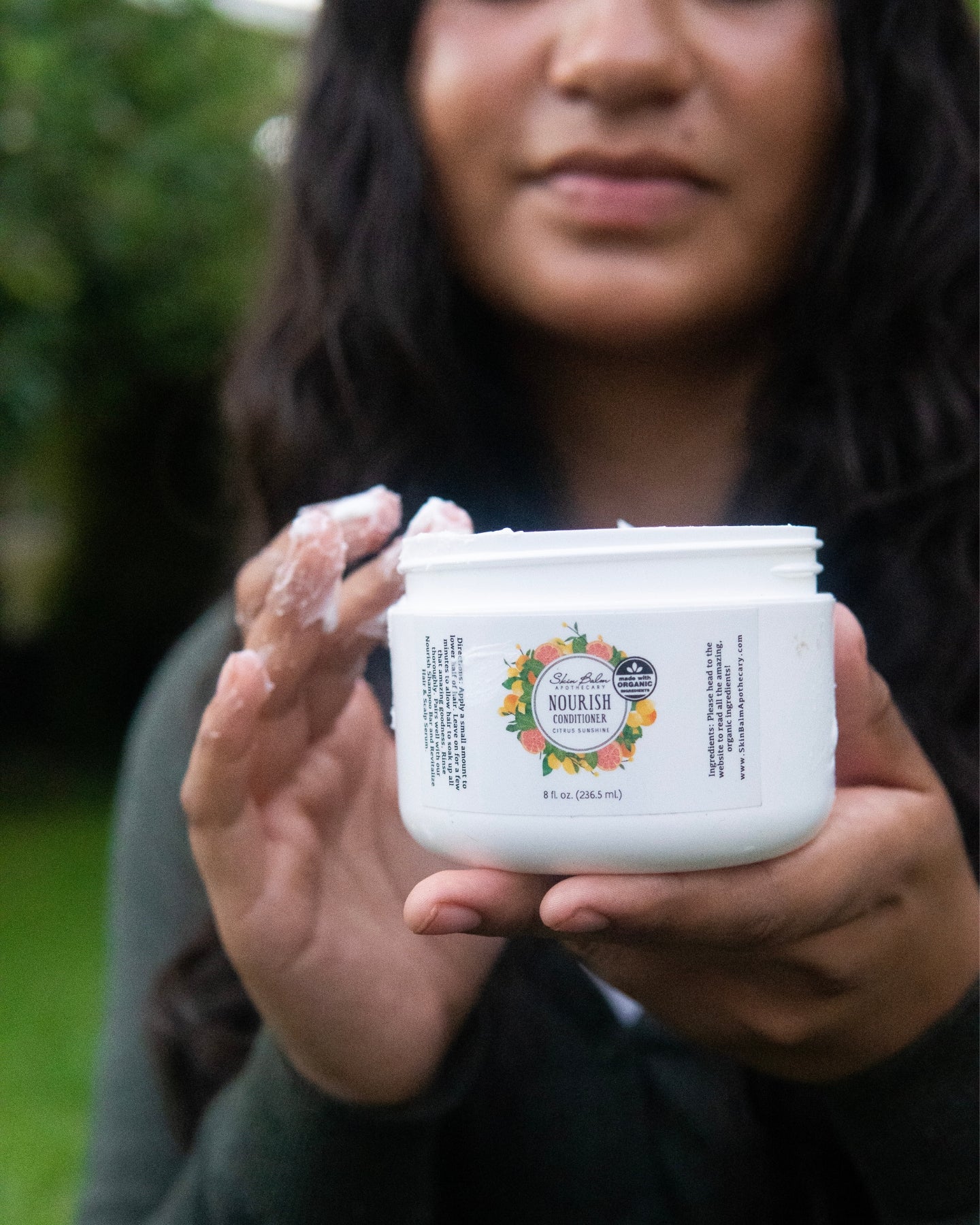 A close-up shot of a woman scooping Citrus Sunshine Nourish Conditioner out of the container.