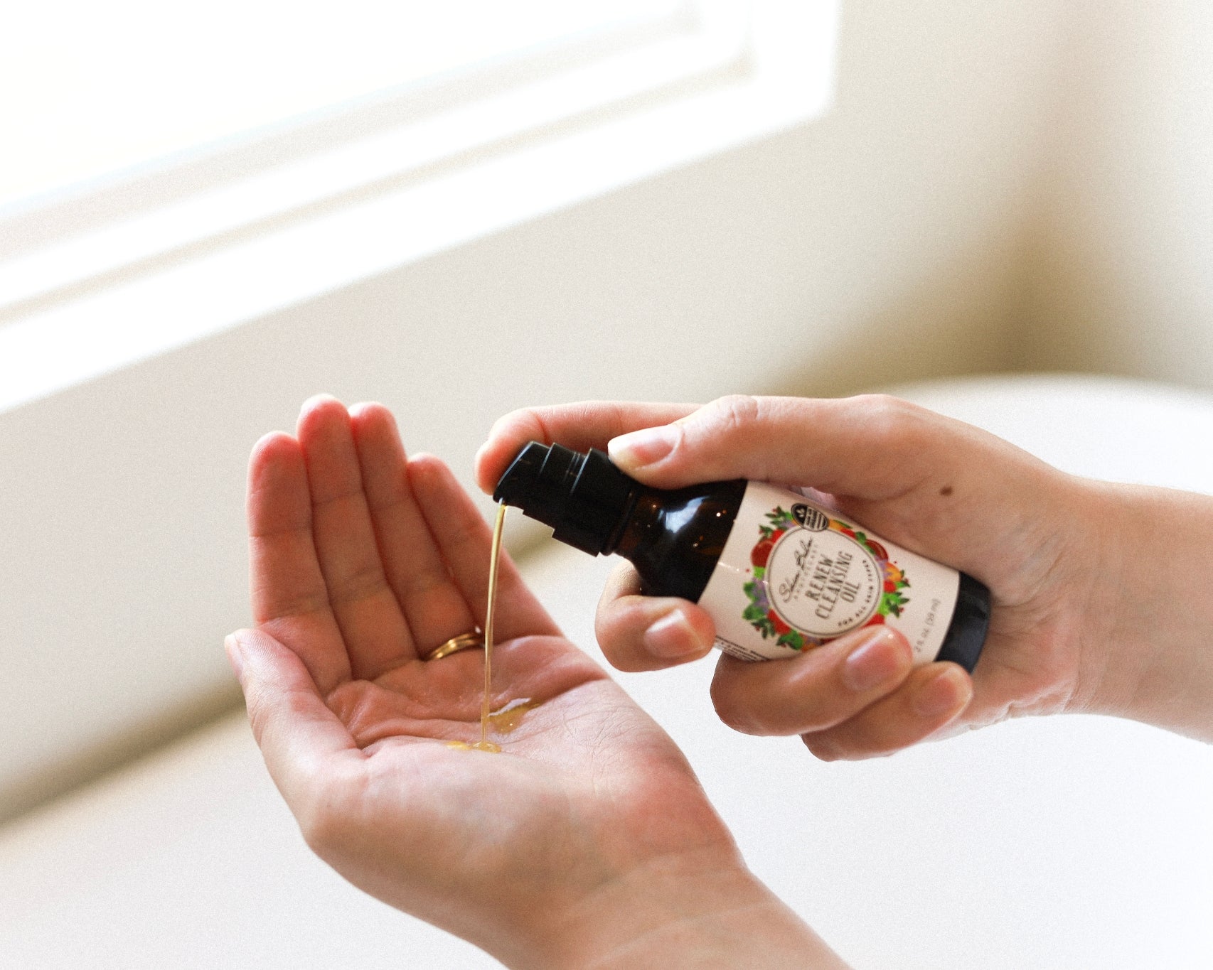 A close-up shot of the Renew Cleansing Oil being squirted into an open palm.